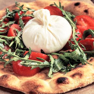 Pane pizza al basilico con insalata di rucola, pomodorini e burrata