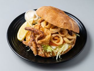 Panino con calamari fritti, insalata, patate fritte e salsa