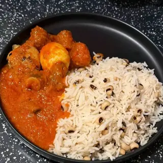 White rice mixed with oloyin beans served with chicken and boiled egg in Nigerian spicy sauce