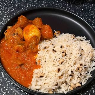 White rice mixed with oloyin beans served with chicken and boiled egg in Nigerian spicy sauce