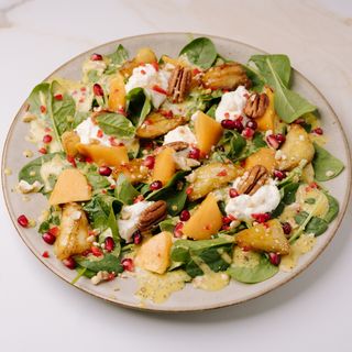 Salată cu spanac proaspăt, kaki, vinete crocante, stracciatella și nuci pecan cu sos de miere și fructul pasiunii