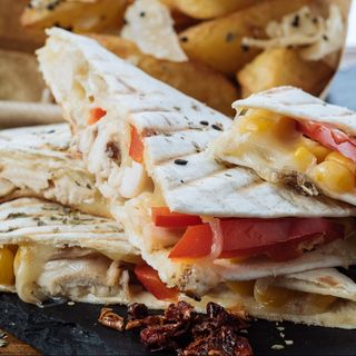 Quesadillia cu pui servită cu cartofi wedges și sos de roșii.