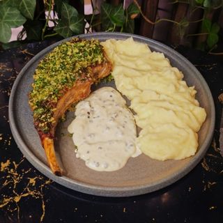 Tomahawk de porc în crustă de verdețuri, cu sos de piper verde și piure de cartofi