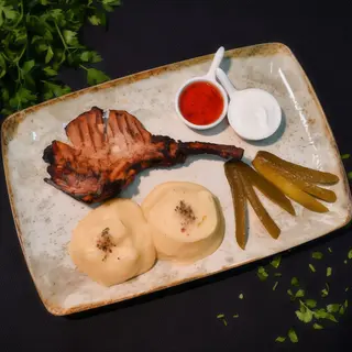 COTLET CU OS - Cotlet de porc cu os(220g) servit alaturi de piure(220g), sos de usturoi cu smantana(30g), sos eros pista cu miere(30g) si castravete murat(50g) - 450g