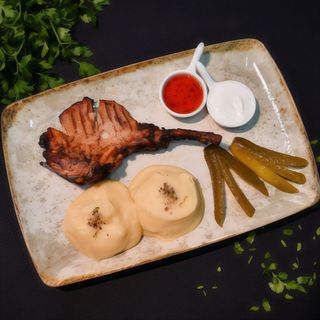 COTLET CU OS - Cotlet de porc cu os(220g) servit alaturi de piure(220g), sos de usturoi cu smantana(30g), sos eros pista cu miere(30g) si castravete murat(50g) - 450g