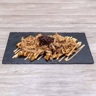 Patate fresche con buccia servite con salsa cheddar piccante, sfilacciata di maiale CBT e cipolla caramellata