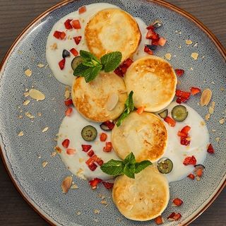 Ніжні сирнички з йогуртовим соусом, сезонними ягодами і горішками