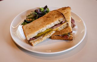 Sándwich de pastrami con queso fundido, mostaza y pepinillos