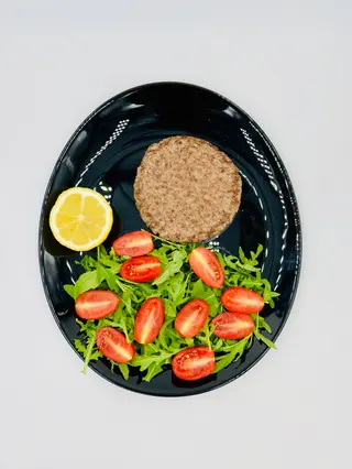 Hamburger di carne alla griglia con rucola, pomodorini e limone