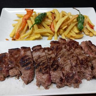 Entrecote troceado sobre patatas y pimientos fritos