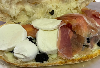 Panino con mozzarella, prosciutto crudo, mozzarella di bufala, pomodorini e olive