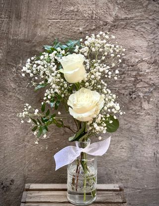 Botella de cristal con dos rosas blancas.