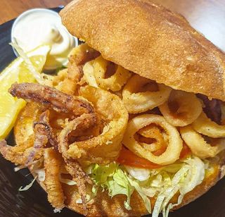 Panino con calamari fritti, insalata, patate fritte e salsa
